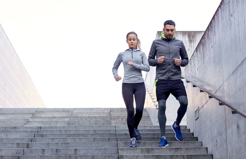Young woman and man jogging down city stairs