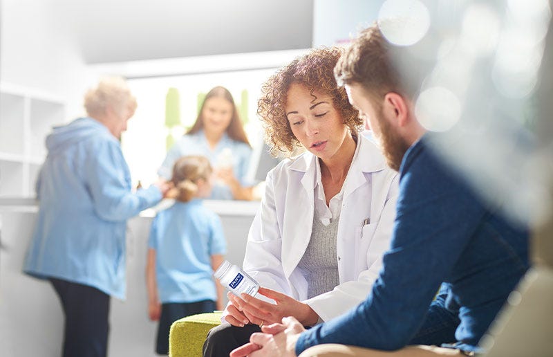 Female healthcare practitioner consulting man on supplements; family in background