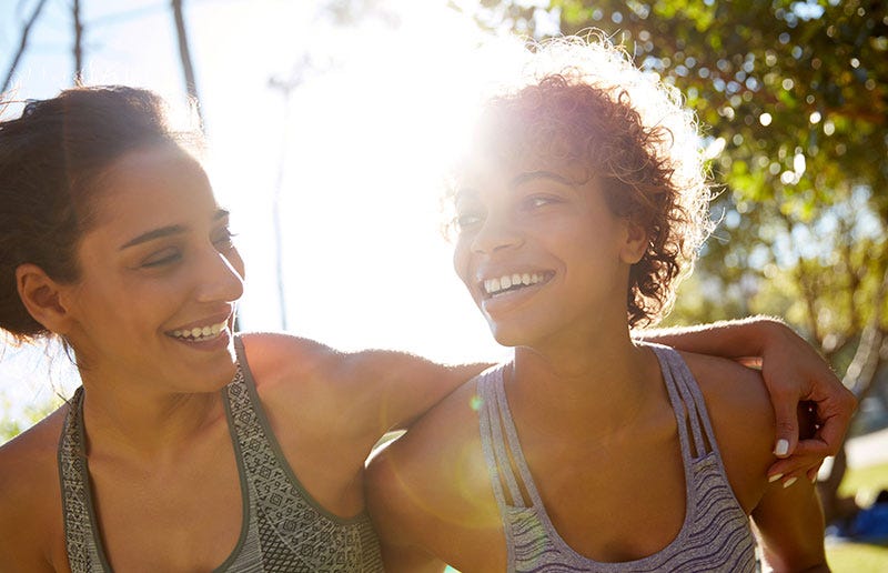 Two women outdoors in athletic wear, smiling in the sunlight