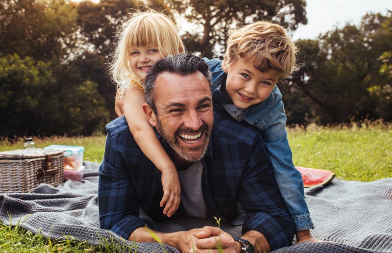 A smiling father relaxing on a picnic blanket with his young children